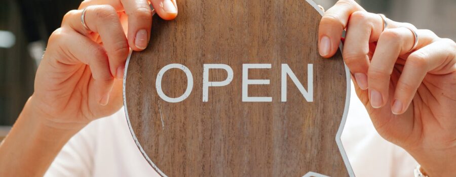 happy woman showing wooden signboard saying open