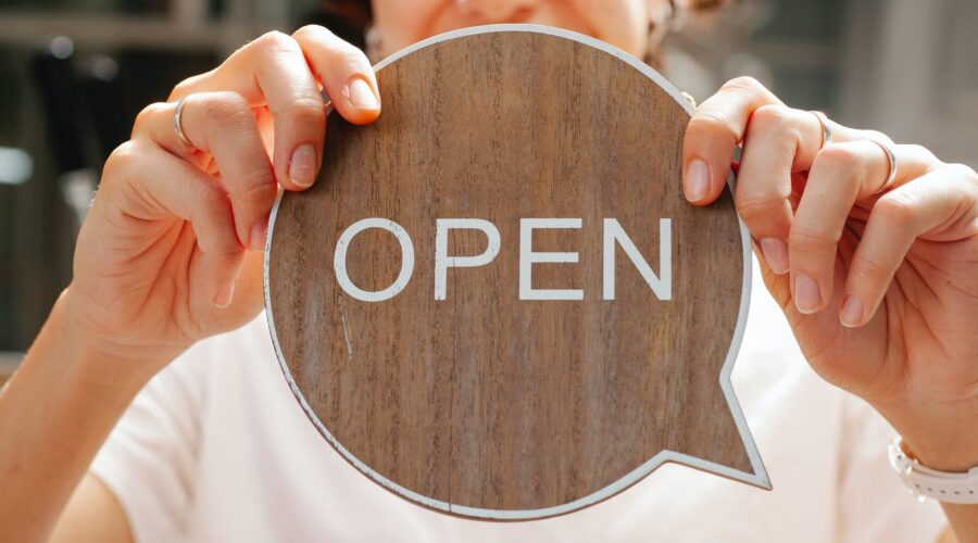 happy woman showing wooden signboard saying open